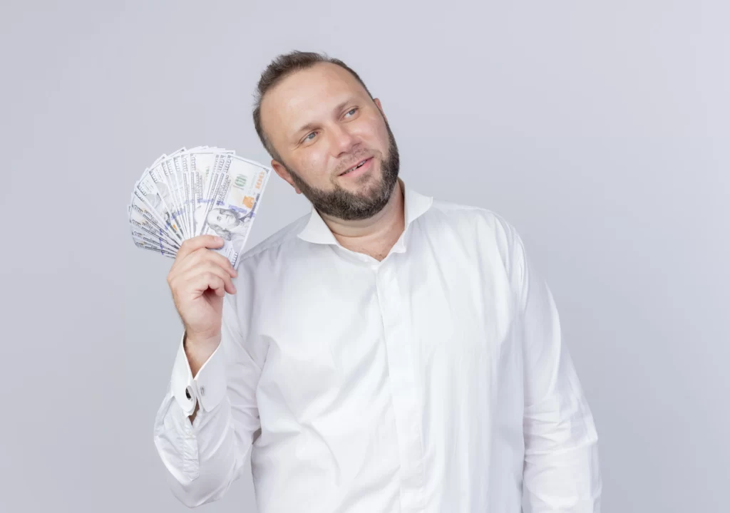 bearded man wearing white shirt holding cash looking aside with confident expression standing white wall