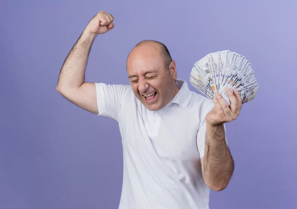 joyful mature businessman holding money raising fist doing yes gesture with closed eyes